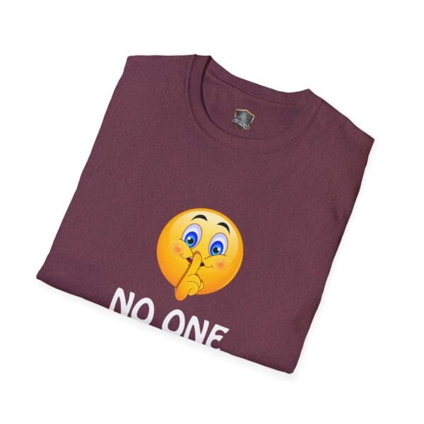 A folded maroon t-shirt featuring an emoji making a shushing gesture and the partially visible text "No One Cares.