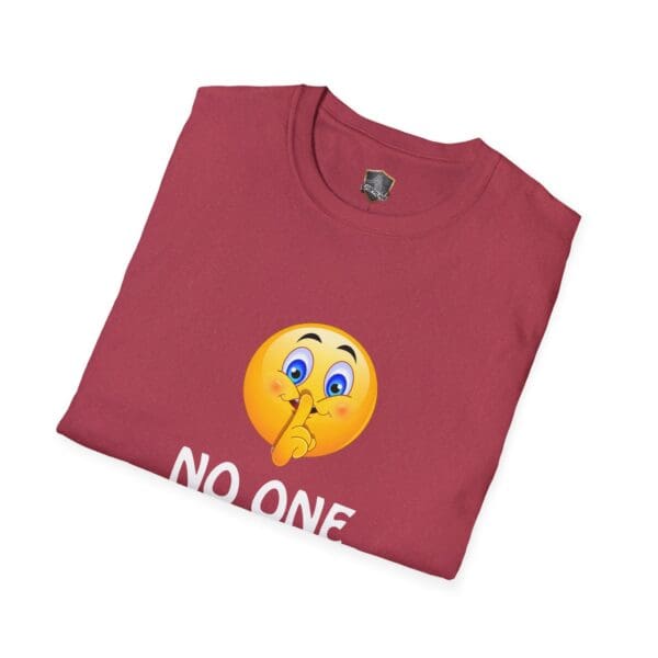 A folded maroon t-shirt featuring a yellow emoji with a finger over its mouth, symbolizing silence. Beneath the emoji, the text reads "NO ONE" from the No One Cares T-Shirt line.