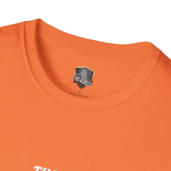 Close-up of an orange "The Man T-Shirt" with a label inside the collar reading "CHIPMUNK" and featuring a shield logo. The material comprises 65% polyester and 35% cotton.