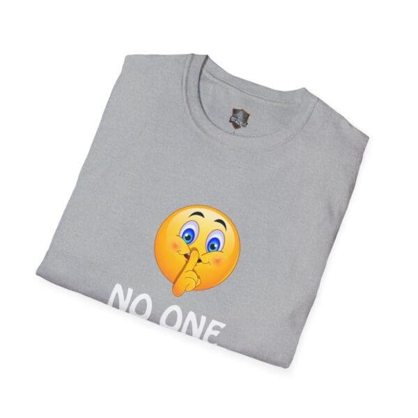 Gray folded "No One Cares" T-shirt featuring an emoji print of a face with a finger over its lips, symbolizing quiet or silence. The words "NO ONE" are partially visible beneath the emoji.