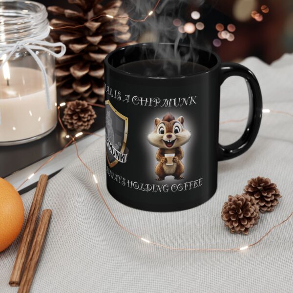 The "My Spirit Animal Is a Chipmunk" Coffee Mug, with a black design depicting a chipmunk holding a coffee cup and a coffee-related caption, sits on a table surrounded by pine cones, an orange, a candle, and string lights.