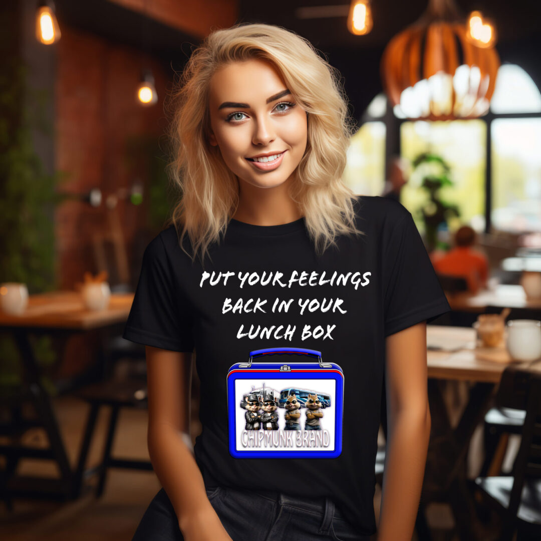 A woman at a cafe sports the Lunchbox Logic Tee, featuring the text "Put your feelings back in your lunch box" alongside an image of a lunch box.